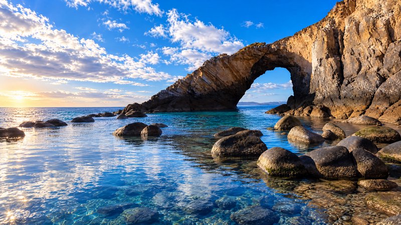 Natural coastal rock arch stands over clear turquoise ocean at golden hour sunset