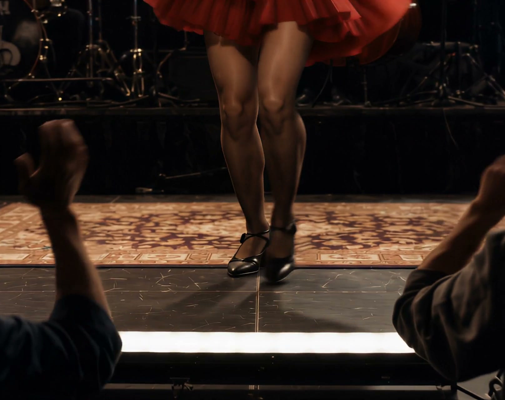 Tap dancer’s legs mid-performance on an indoor stage, with audience members’ raised cheering hand...