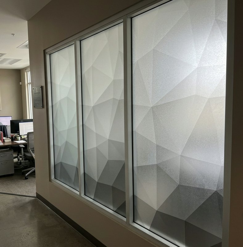 Geometric gradient frosted privacy film on glass office partition next to a modern office hallway