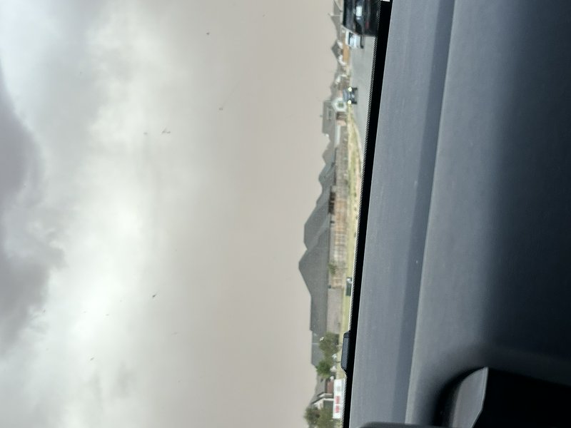 View from inside a car of an approaching tan dust storm rolling over a residential suburban neigh...