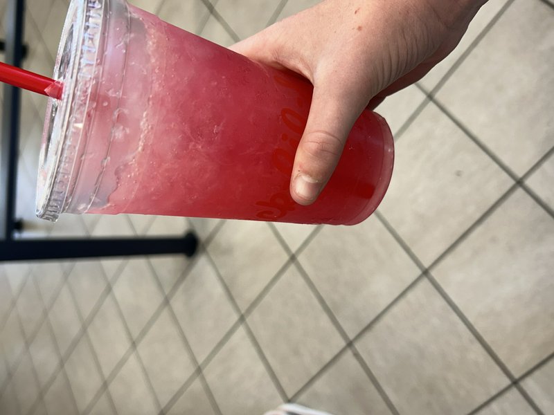 Hand holding a condensation-covered Chick-fil-A plastic cup filled with bright red iced frozen dr...