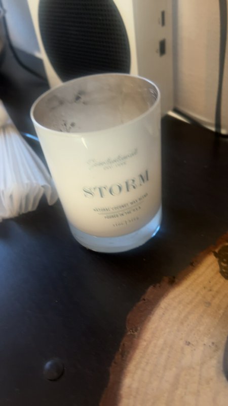 Partially burned white glass "STORM" scented candle jar resting on a black live-edge home office ...