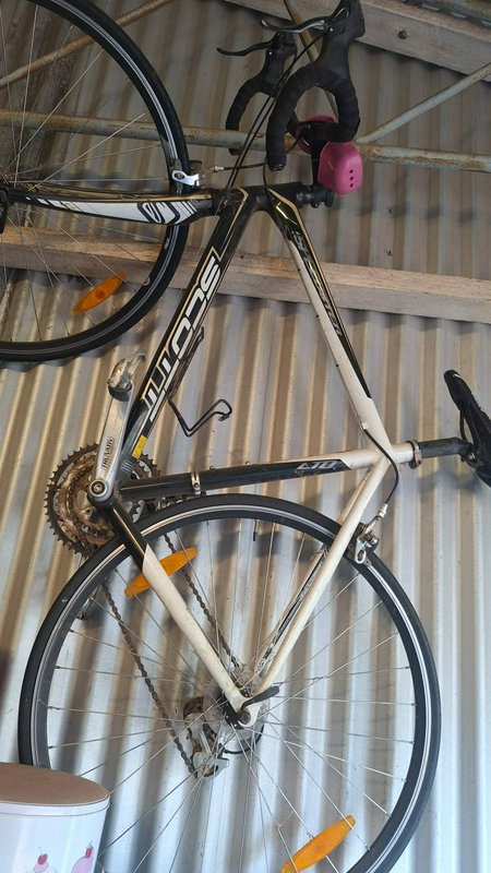 Two Scott road bicycles hanging from a wooden storage rack mounted to a corrugated metal shed wall.