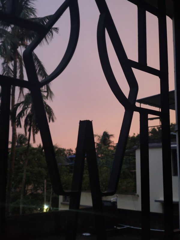 Silhouetted geometric metal railing framing a sunset with palm trees.