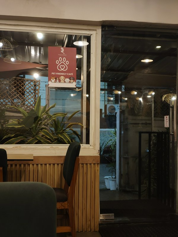 Glass entry of a cozy pet-friendly cafe, with a maroon 'Pet Friendly Cafe' paw print sign, indoor...