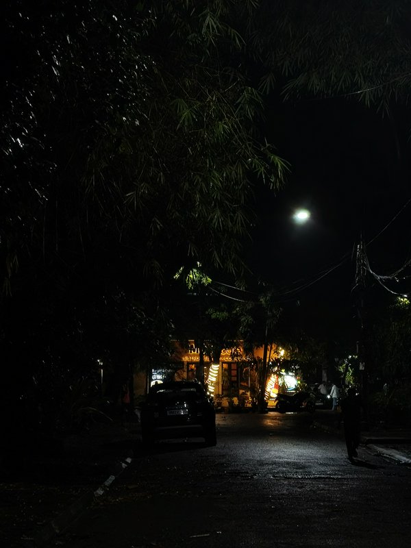 Quiet nighttime Indian residential street with a lit neighborhood shop, parked car, pedestrian, o...