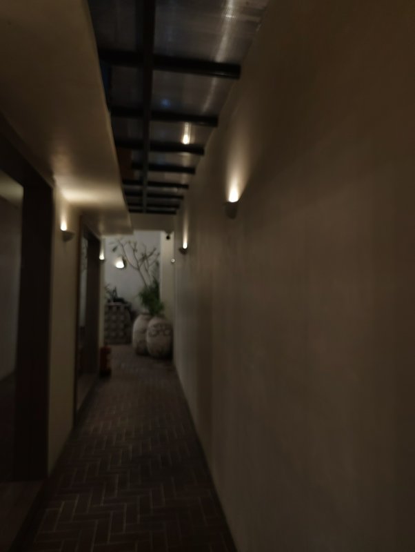 Dimly lit modern interior hallway with wall sconce lighting, herringbone tile floors, and potted ...