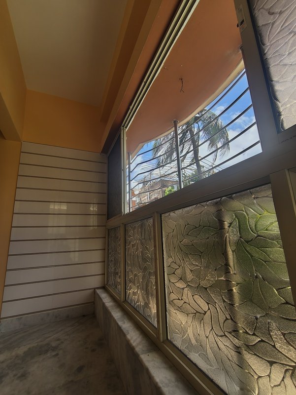 Sunlit apartment balcony nook with leaf-pattern frosted glass windows overlooking palm trees and ...