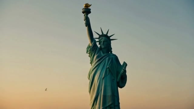 Low angle shot of the Statue of Liberty standing against a soft warm gradient sunset sky, with a ...