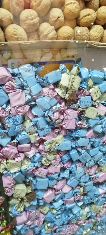 Close-up of bulk pastel foil-wrapped candies in a display bin, with in-shell walnuts stacked on t...