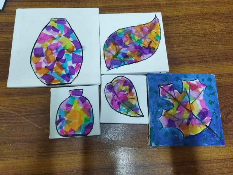 Five small stained-glass style painted mini canvases with leaf and vase designs rest on a wooden ...