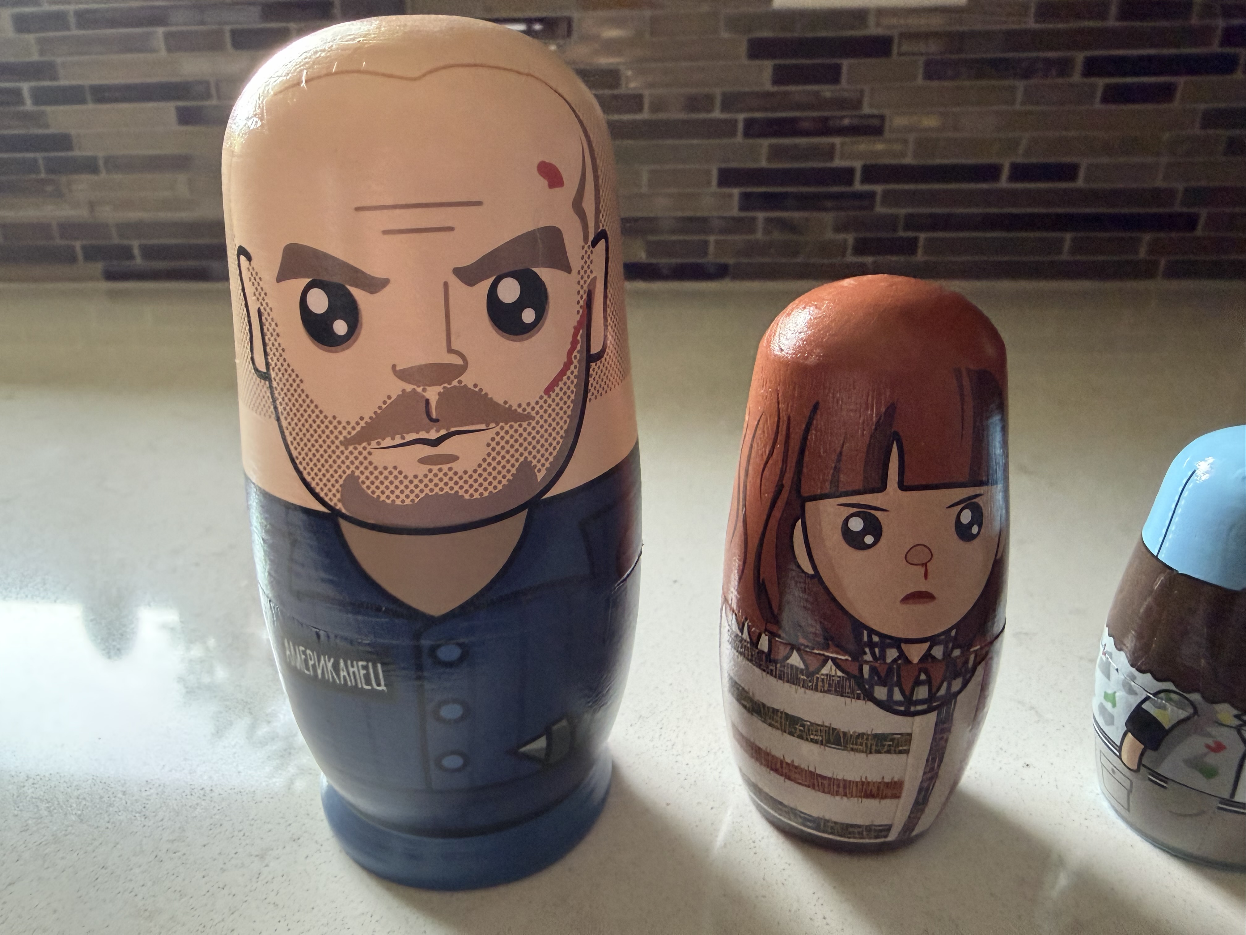 Three illustrated wooden nesting dolls featuring a bearded man, a girl, and a small figure on a kitchen counter.