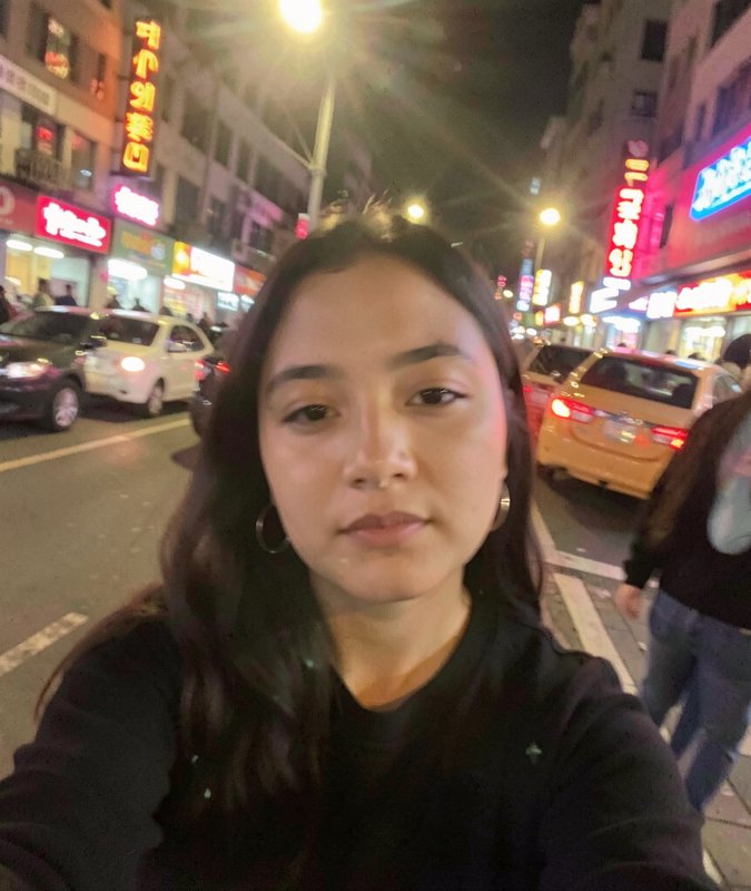 Young woman taking a nighttime street selfie in a neon-lit city.
