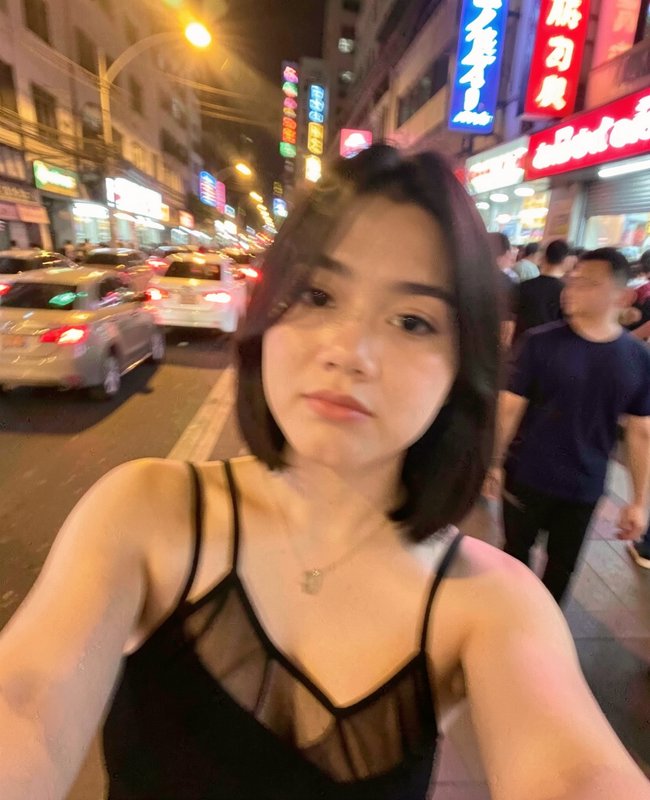 Young woman taking a selfie on a busy neon-lit downtown city street at night, with traffic and gl...