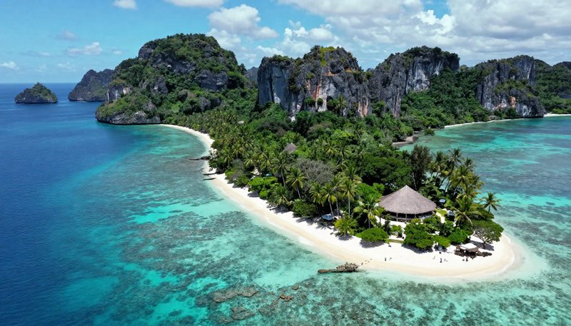 Aerial view of secluded tropical island resort with white sand beach, palm trees, jagged limeston...