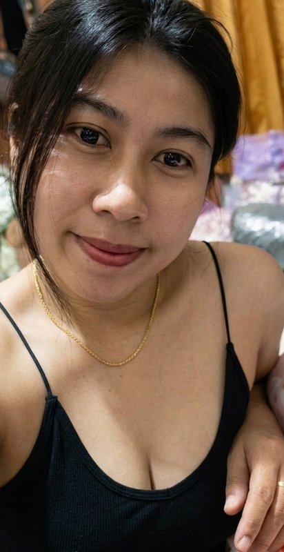 Close-up portrait of a smiling Southeast Asian woman in a black camisole with a thin gold necklac...