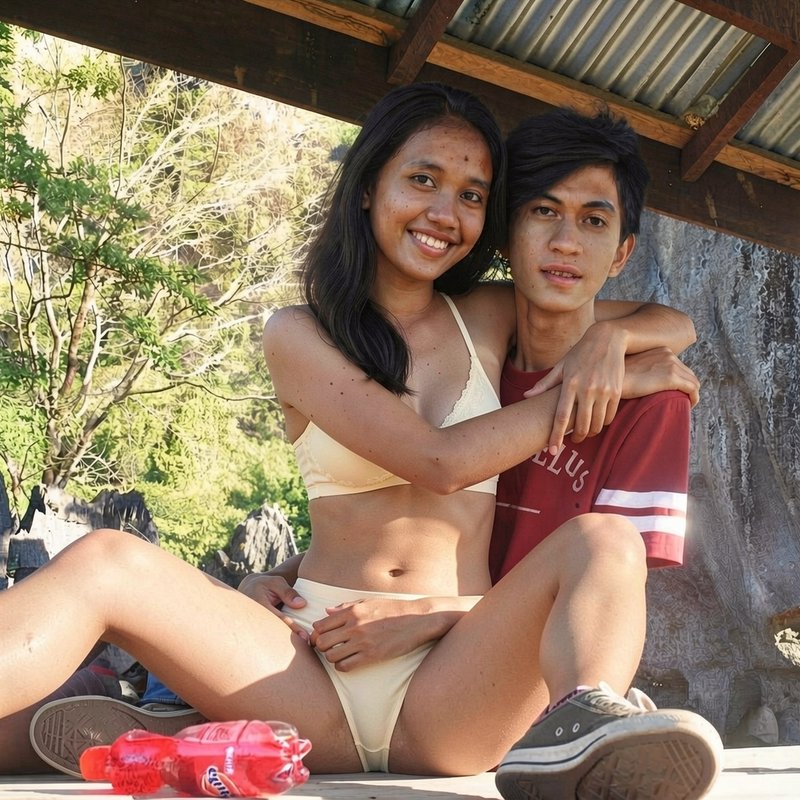 Smiling young Southeast Asian couple embrace while sitting together under a shaded outdoor shelte...