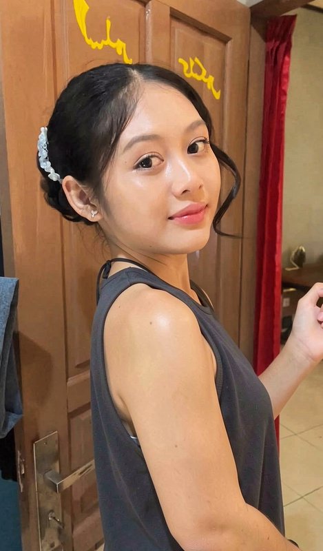 Young woman with a beaded hair clip looks over her shoulder standing indoors