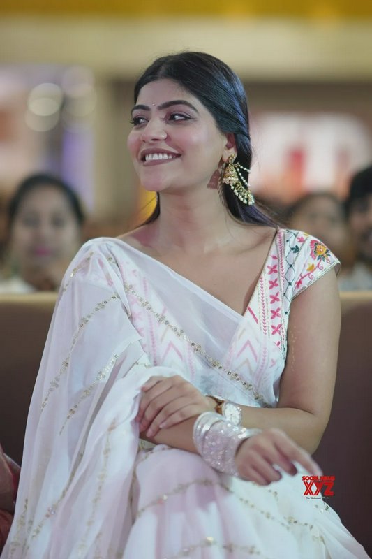 Smiling South Indian actress Manjima Mohan in a white embroidered saree, seated at a public event...