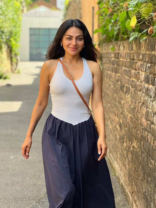 Smiling woman with long dark hair walks along a sunlit residential brick alley in casual summer a...