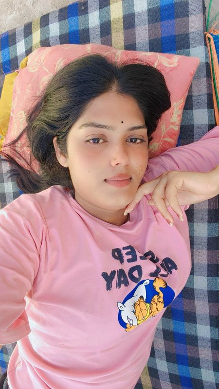 Young South Asian woman takes a casual selfie lying on a checkered mat wearing a pink Garfield pr...