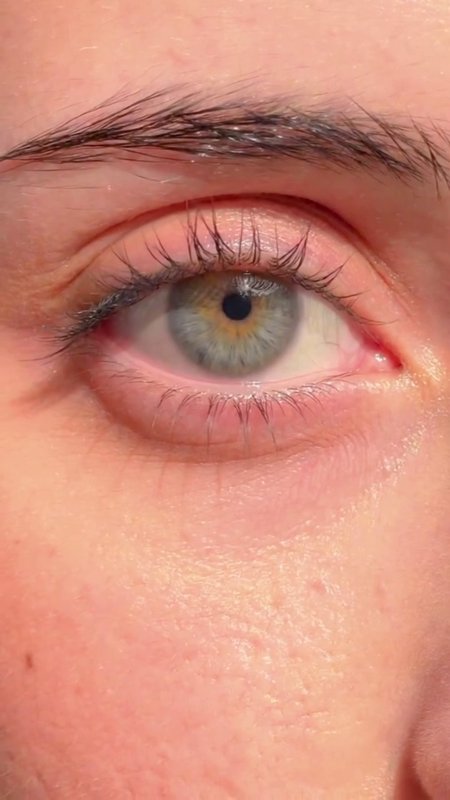 Extreme close up of a natural human eye with a pale grey hazel iris, dark eyebrow, and dewy light...