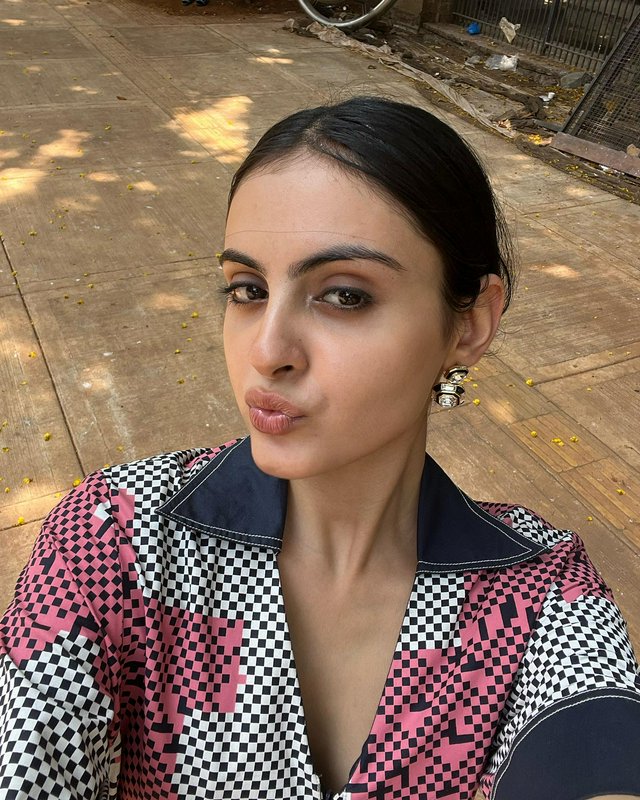 Candid outdoor selfie of young South Asian woman in a geometric checkered collared top, pouting p...