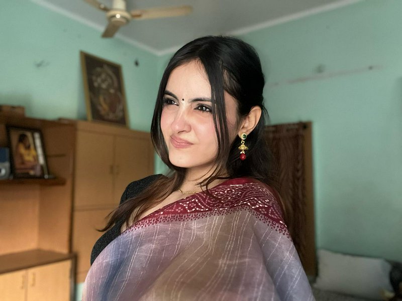 Candid portrait of a young Indian woman in a gradient saree with traditional jewelry, inside a co...