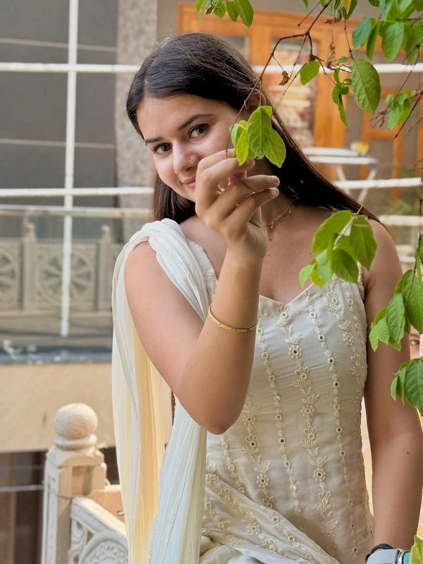 Young South Asian woman in embroidered off-white ethnic wear holds green tree leaves, smiling sof...