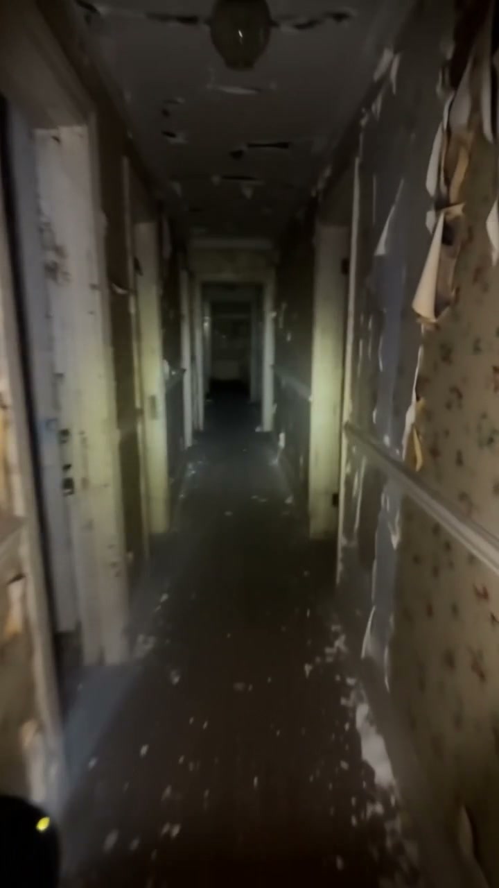 Dilapidated narrow hallway in an abandoned building with peeling wallpaper and crumbling ceiling