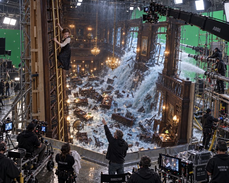Behind-the-scenes on a film set: actress climbs library ladder as crew shoots elaborate practical...