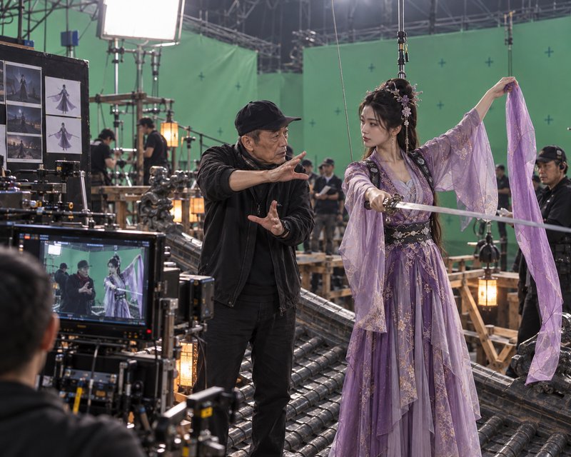 Director guides an actress holding a sword on a green screen fantasy film set