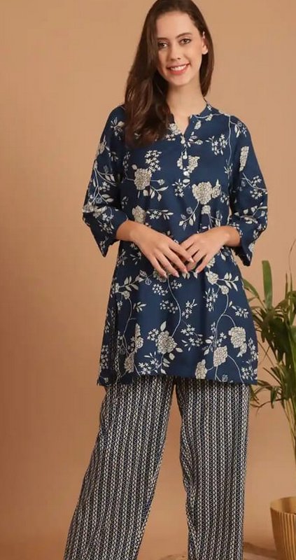 Smiling model wearing a navy blue floral print tunic co-ord loungewear set against a warm tan stu...