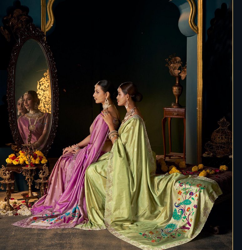 Two women in embroidered traditional Indian sarees sit beside an ornate vintage mirror in a royal...