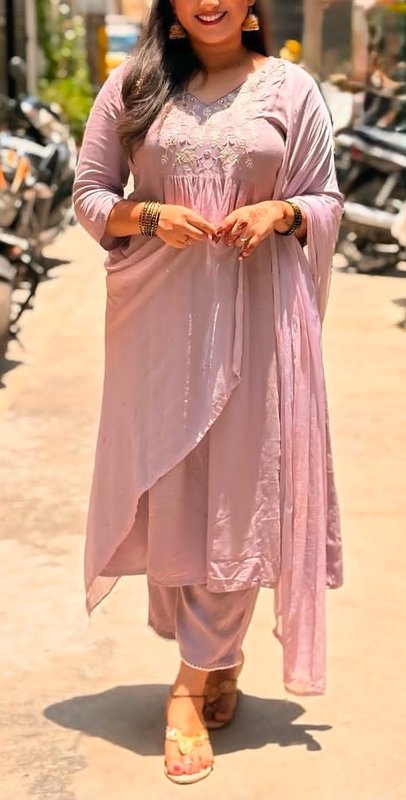 Woman wearing a soft lavender embroidered Indian kurta suit with traditional jewelry, standing on...