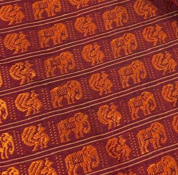 Close up of woven traditional fabric with repeating orange elephant and bird motifs on a deep mar...