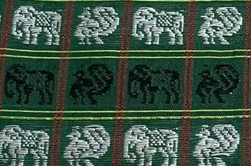 Close up of woven traditional textile with repeating elephant and peacock motifs on dark green st...