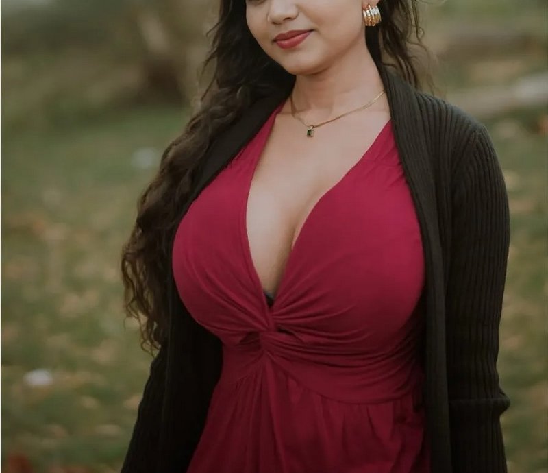 Cropped upper body portrait of a woman in a burgundy dress and black cardigan standing in a blurr...