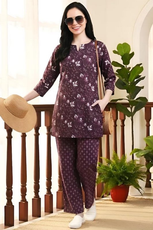 Smiling woman models a dark purple floral print co-ord loungewear set on a sunlit home balcony