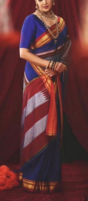 Woman in royal blue and maroon handwoven silk saree wearing gold temple jewelry against a red dra...