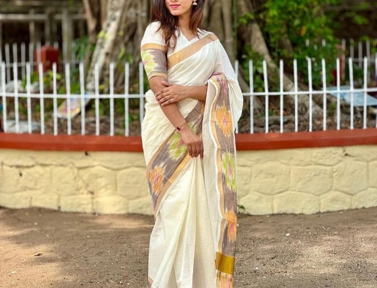Woman wearing an elegant off-white Kerala handloom saree with ikat border stands outdoors in a su...