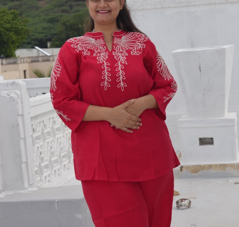 Smiling woman in a bright red embroidered co-ord set standing on a white residential rooftop