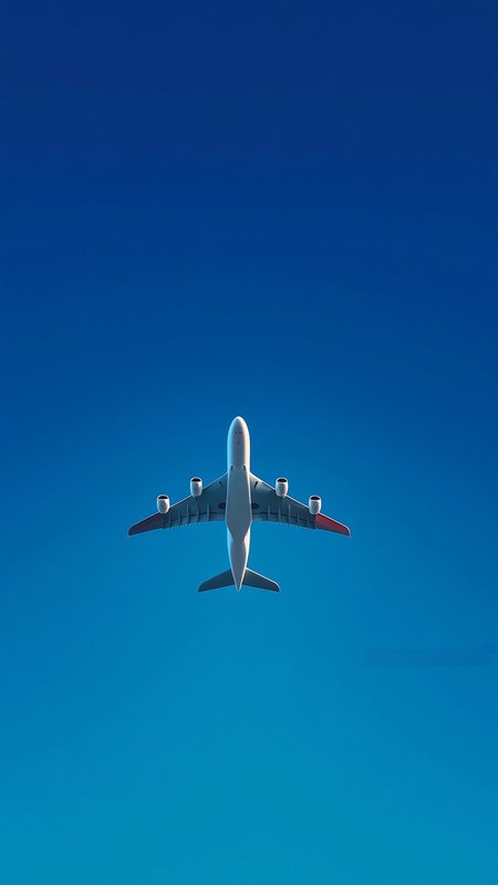 Low angle upward view of a four-engine wide-body commercial airliner flying against a clear gradi...