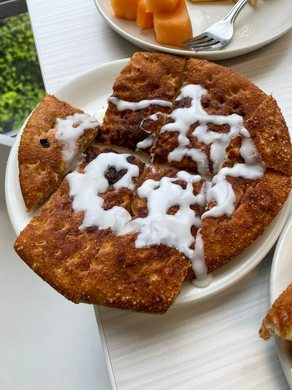 Sliced warm cinnamon pastry drizzled with white icing, served on a plate with a side of fresh cut...