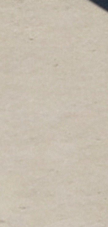 Close-up of matte pale beige speckled textured surface, dotted with faint taupe flecks and a smal...