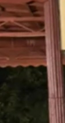 Blurry low-angle view of warm wooden porch roof framing, fluted support post, and dark treetops a...