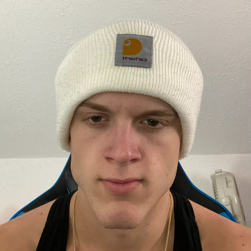 Closeup fisheye selfie of a young man wearing a white Carhartt knit beanie, with deadpan expressi...