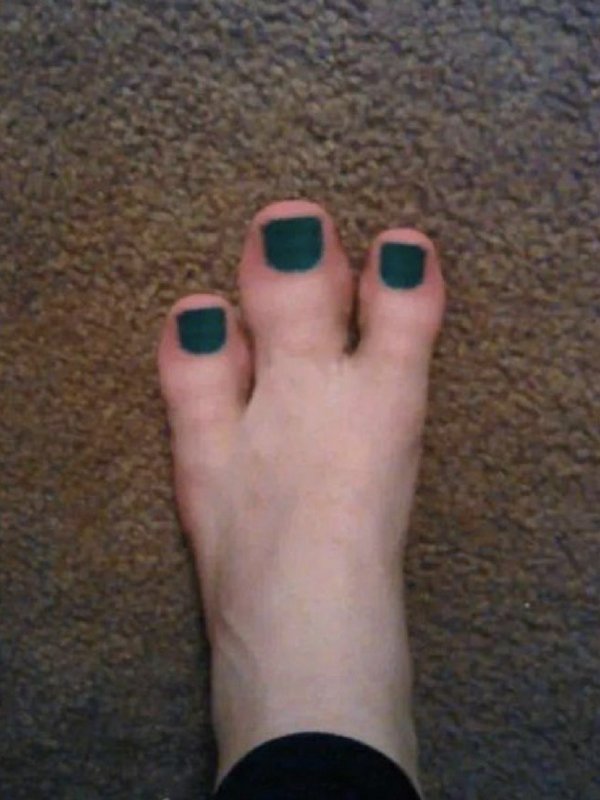 Top down view of a foot with dark forest green toenail polish resting on textured brown plush carpet
