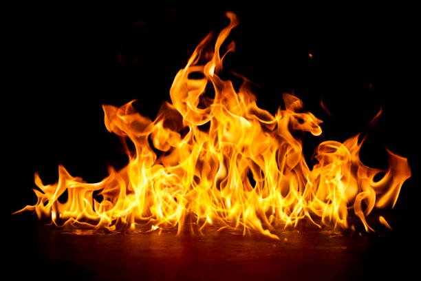 Bright swirling orange and yellow fire flames flicker dynamically against a solid pure black back...