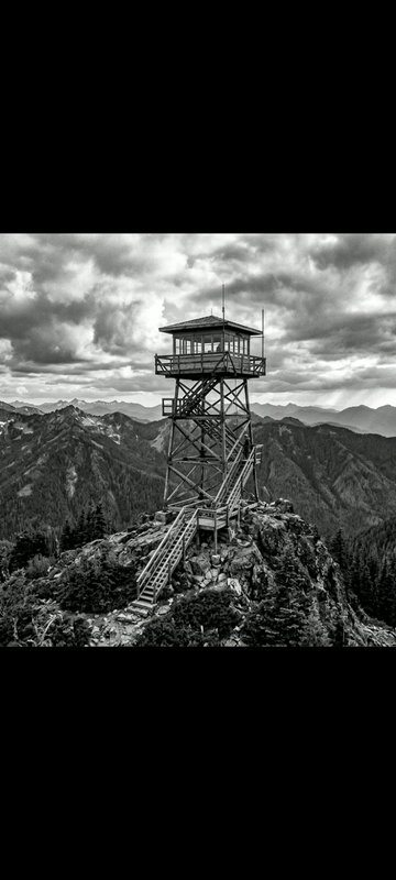 Wooden fire lookout tower perched on a rocky mountain peak under dramatic cloudy skies